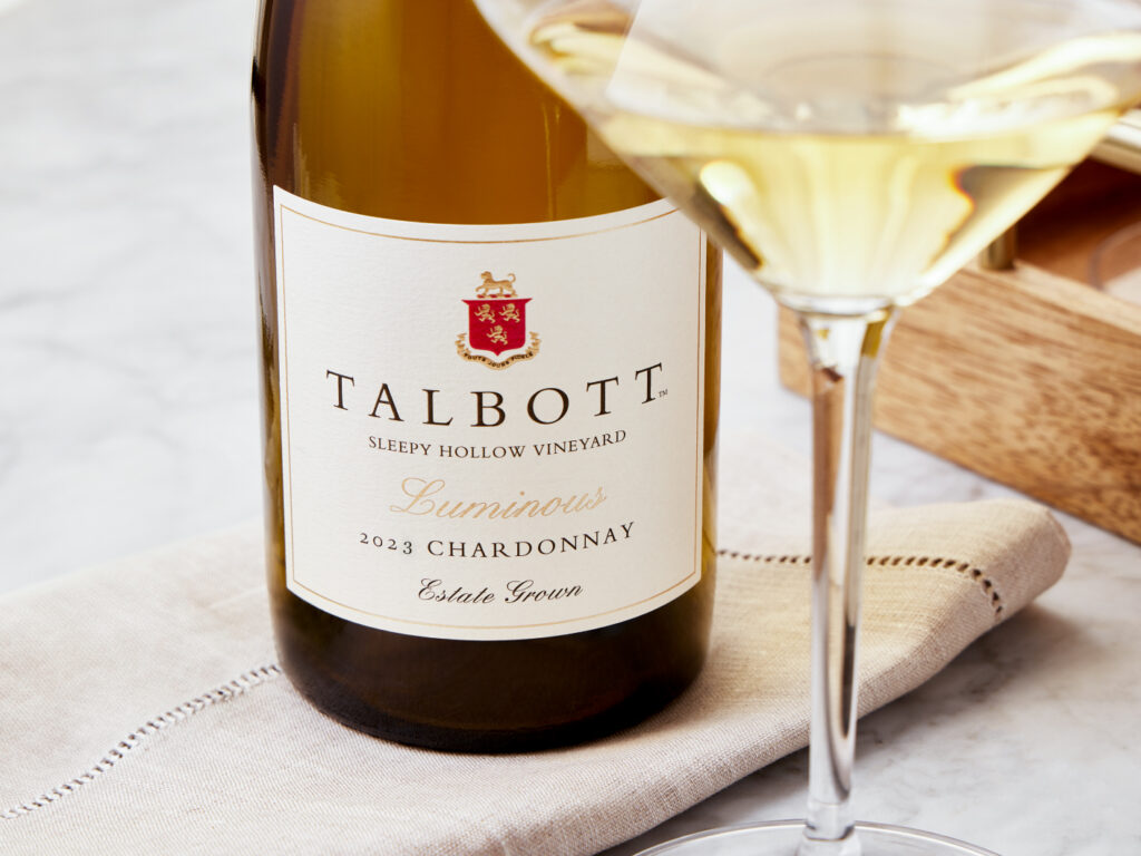 A bottle of Talbot Vineyards Luminous Chardonnay placed on a napkin beside a wine glass.